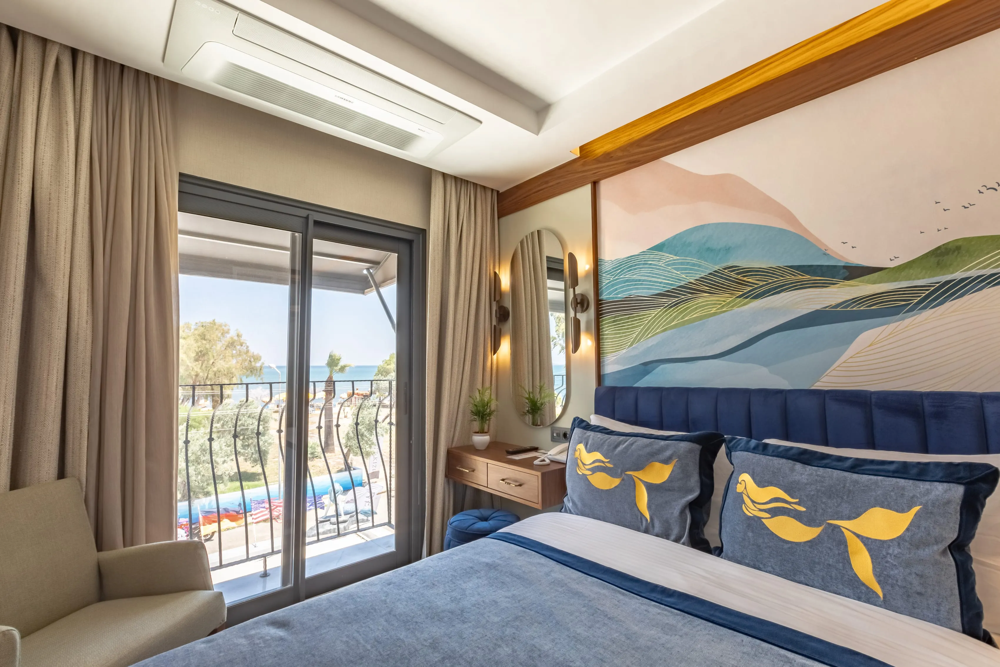 Ein Zimmer mit Balkontür: ein marineblaues Kopfteil, das Wellen-Wandbild und draußen das Meer