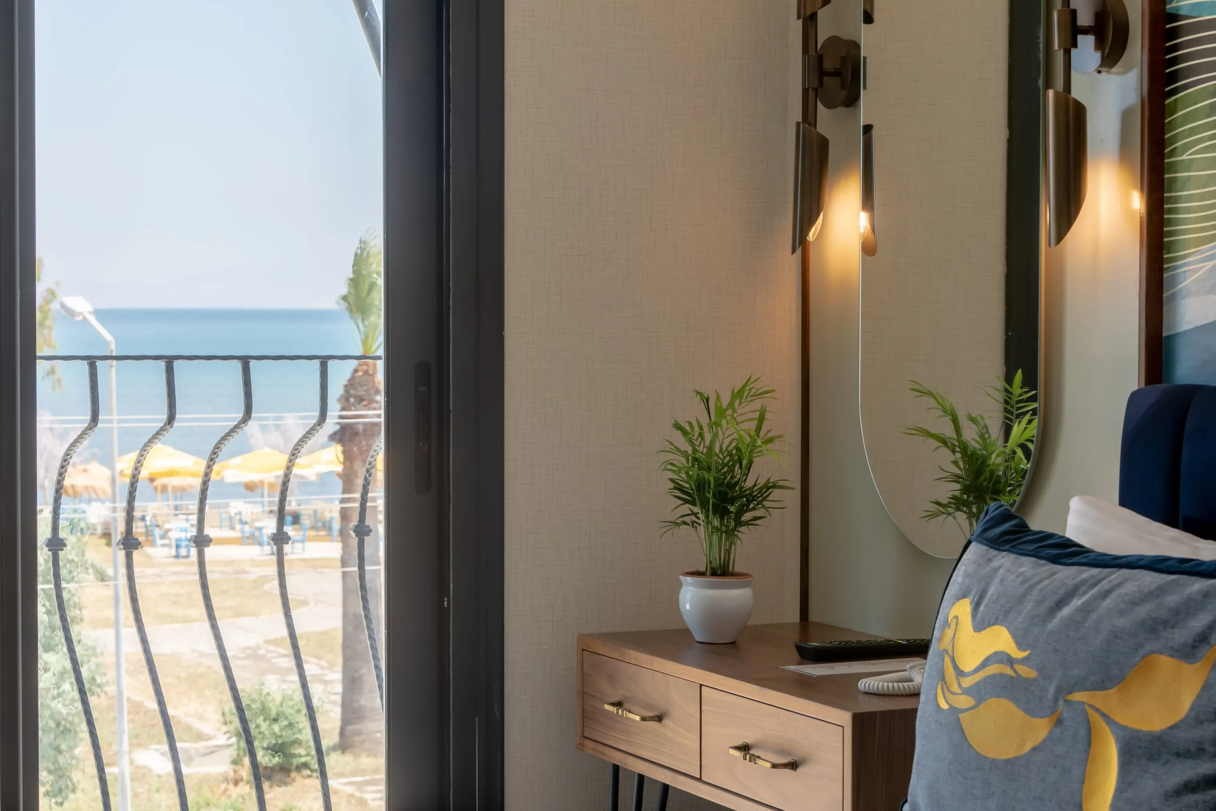 The wave-forged balcony rail with the sea behind it; beside it a potted plant, an oval mirror and a mermaid cushion