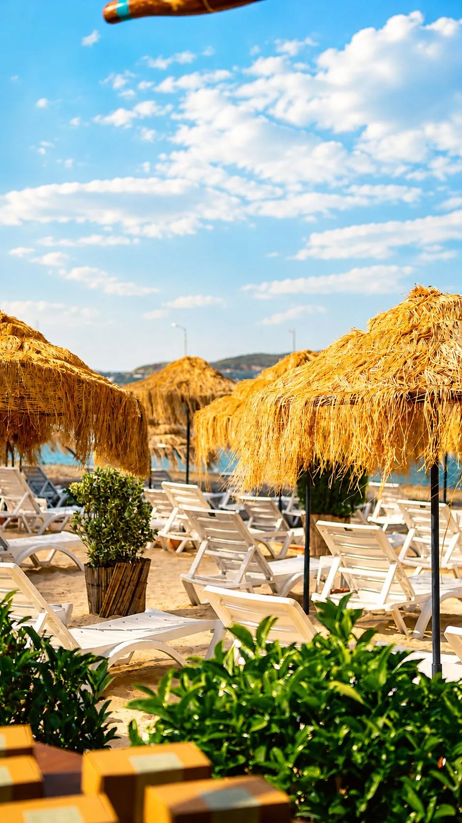 Strohschirme und weiße Liegen am Strand von Deniz Kızı Urla; dahinter das Wasser der Bucht und offener Himmel