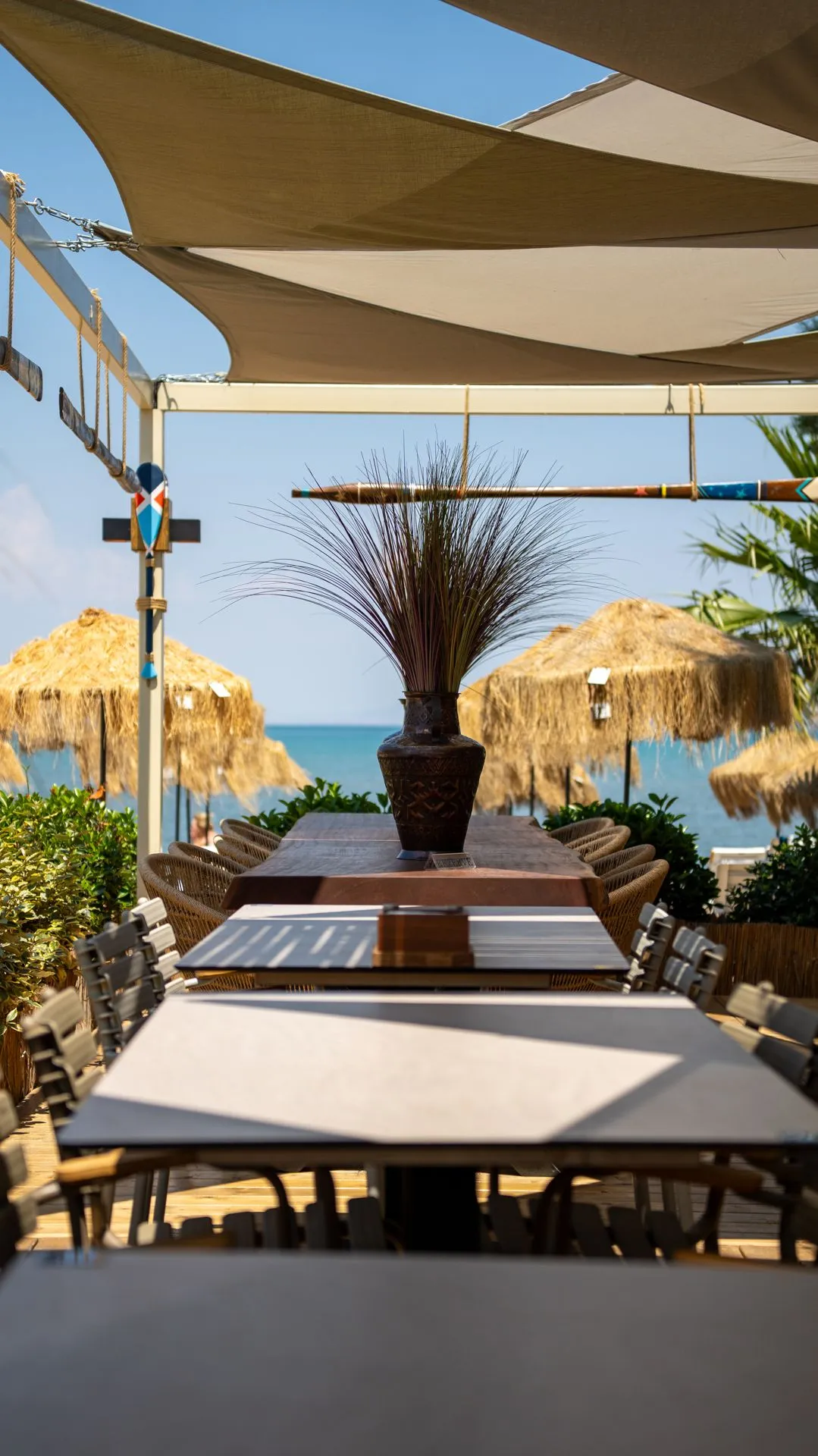 A long table set under a canopy; straw parasols and the sea horizon of the cove behind
