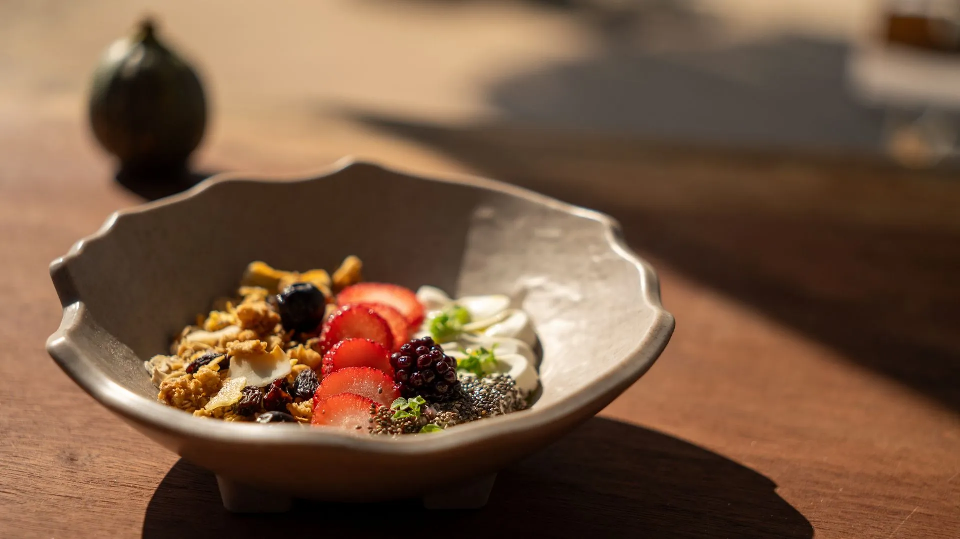Granola, Erdbeeren, Brombeeren und Joghurt in einer Keramikschale; auf einem Holztisch