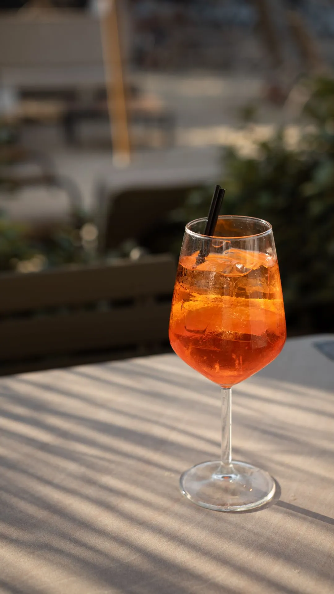 Ein orangefarbener Cocktail mit Eis und Orangenscheibe auf einem Tisch mit Streifenschatten