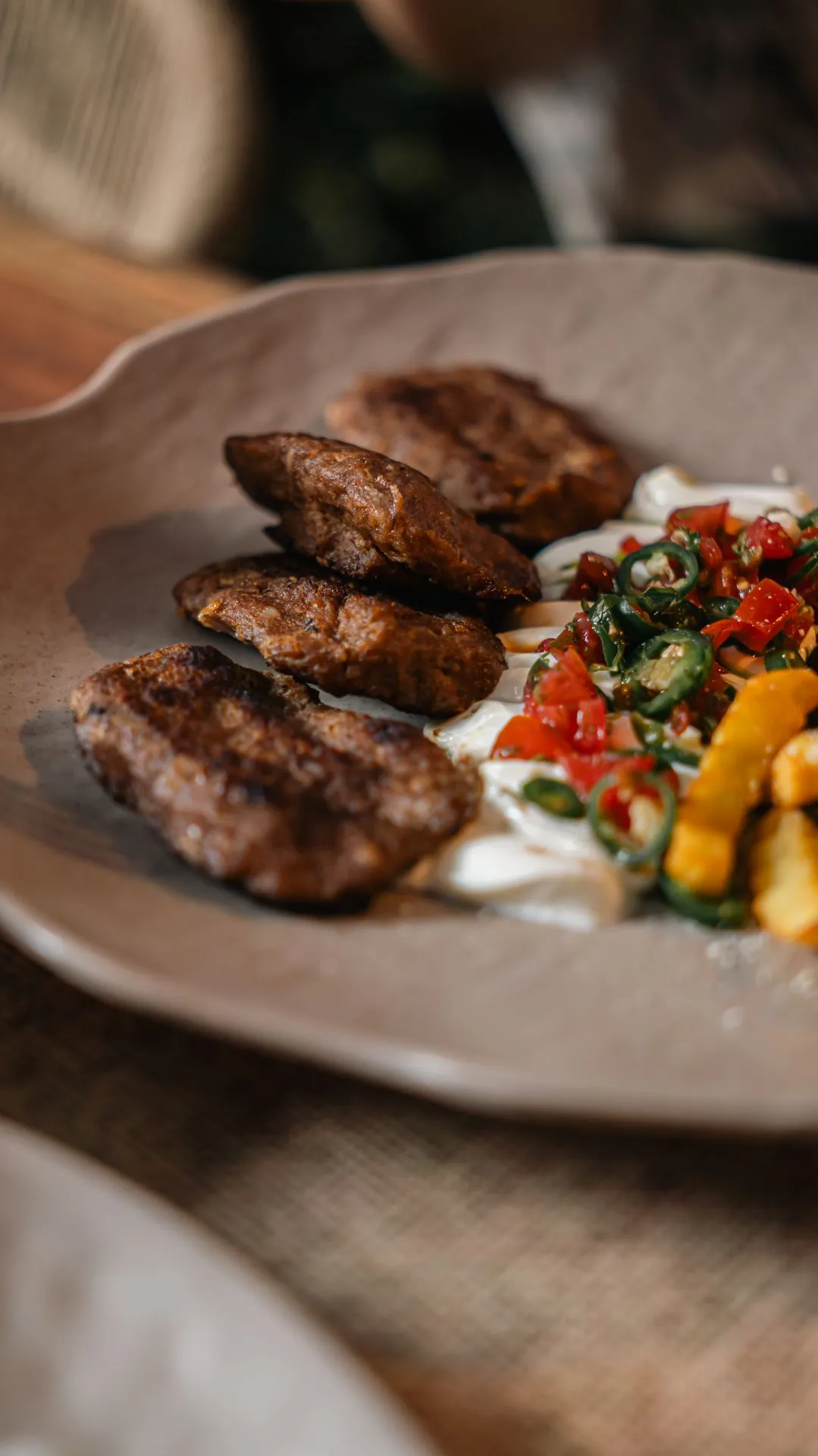 Gegrillte Köfte auf einem Teller mit Joghurt und einer Tomaten-Paprika-Beilage
