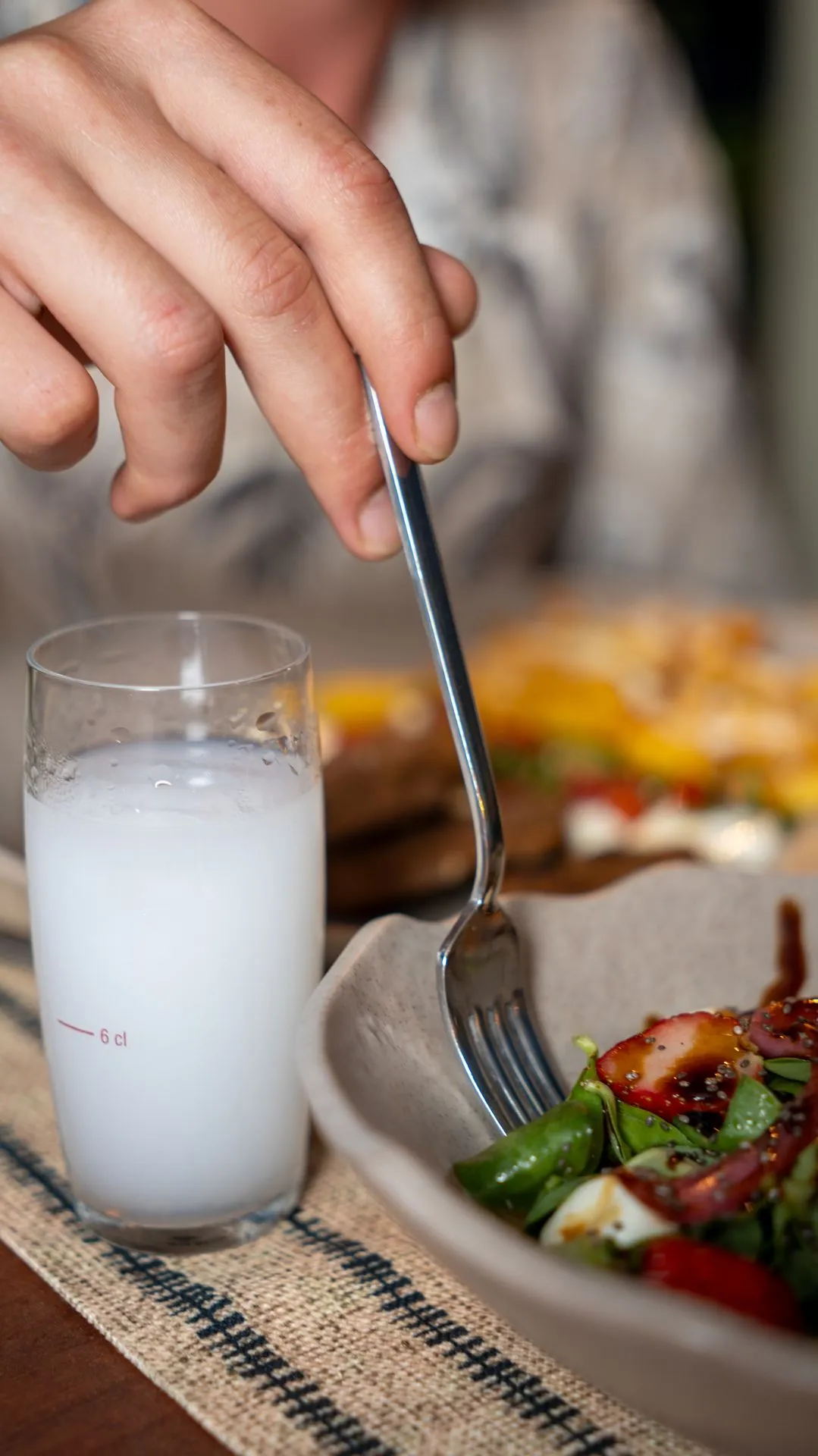 Eine Hand greift mit der Gabel in einen Erdbeersalat; daneben ein trübes weißes Getränk