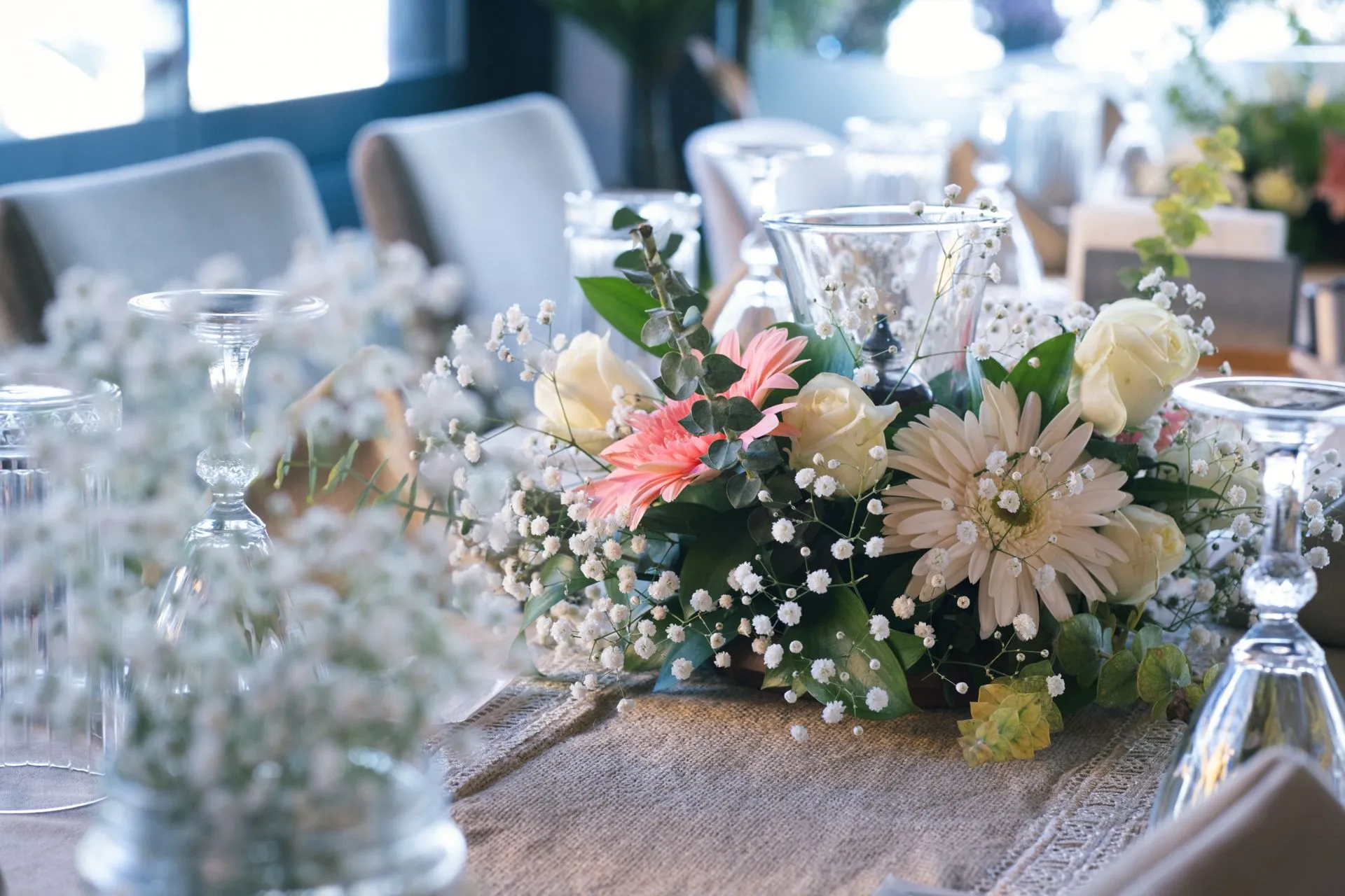 Eine Nahaufnahme des Blumengestecks in der Tischmitte: cremefarbene Rosen, Puder-Gerbera, Schleierkraut und Grün