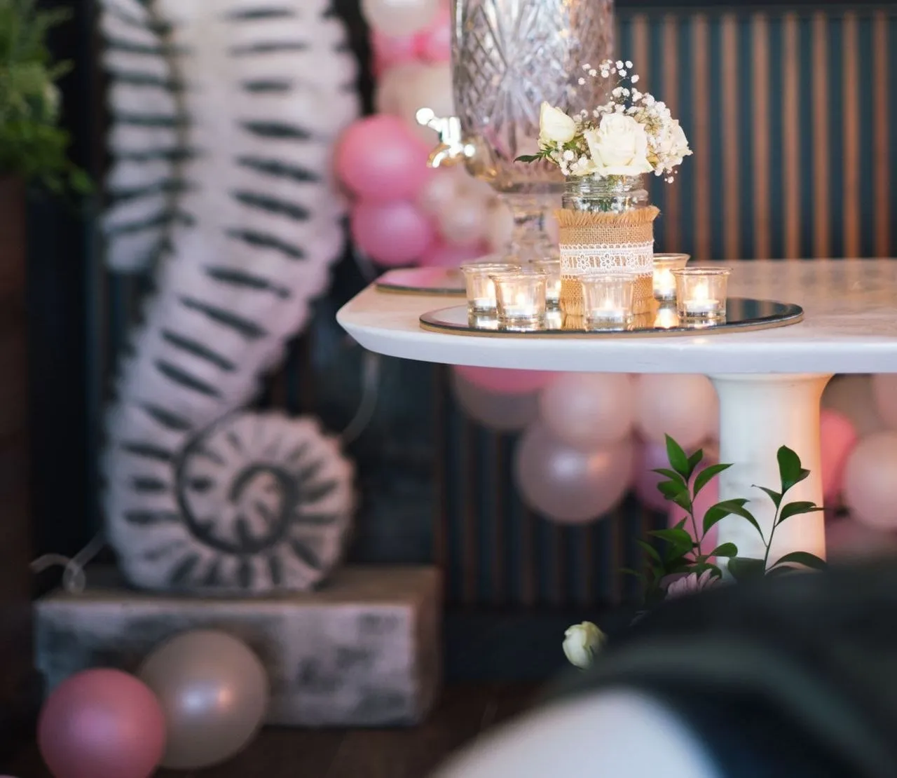 Eine weiße Seepferdchenskulptur neben einem Festtisch; auf dem Tisch Glasgefäße, Kerzen und Blumen, darunter rosa Luftballons