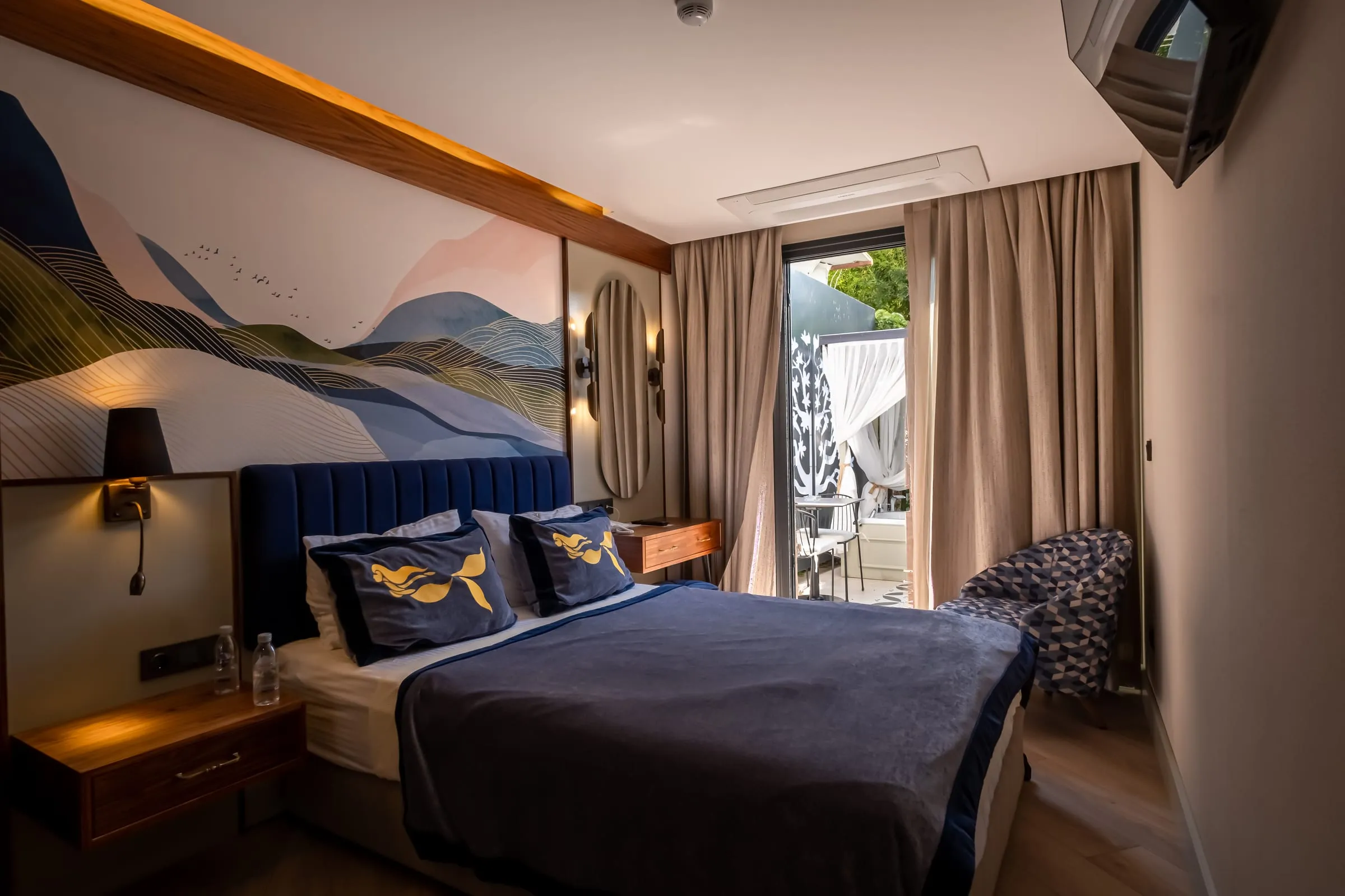 Das Zimmer im Abendlicht: das Samtkopfteil, Meerjungfrau-Kissen, eine Nachttischlampe und das Voile auf dem Balkon