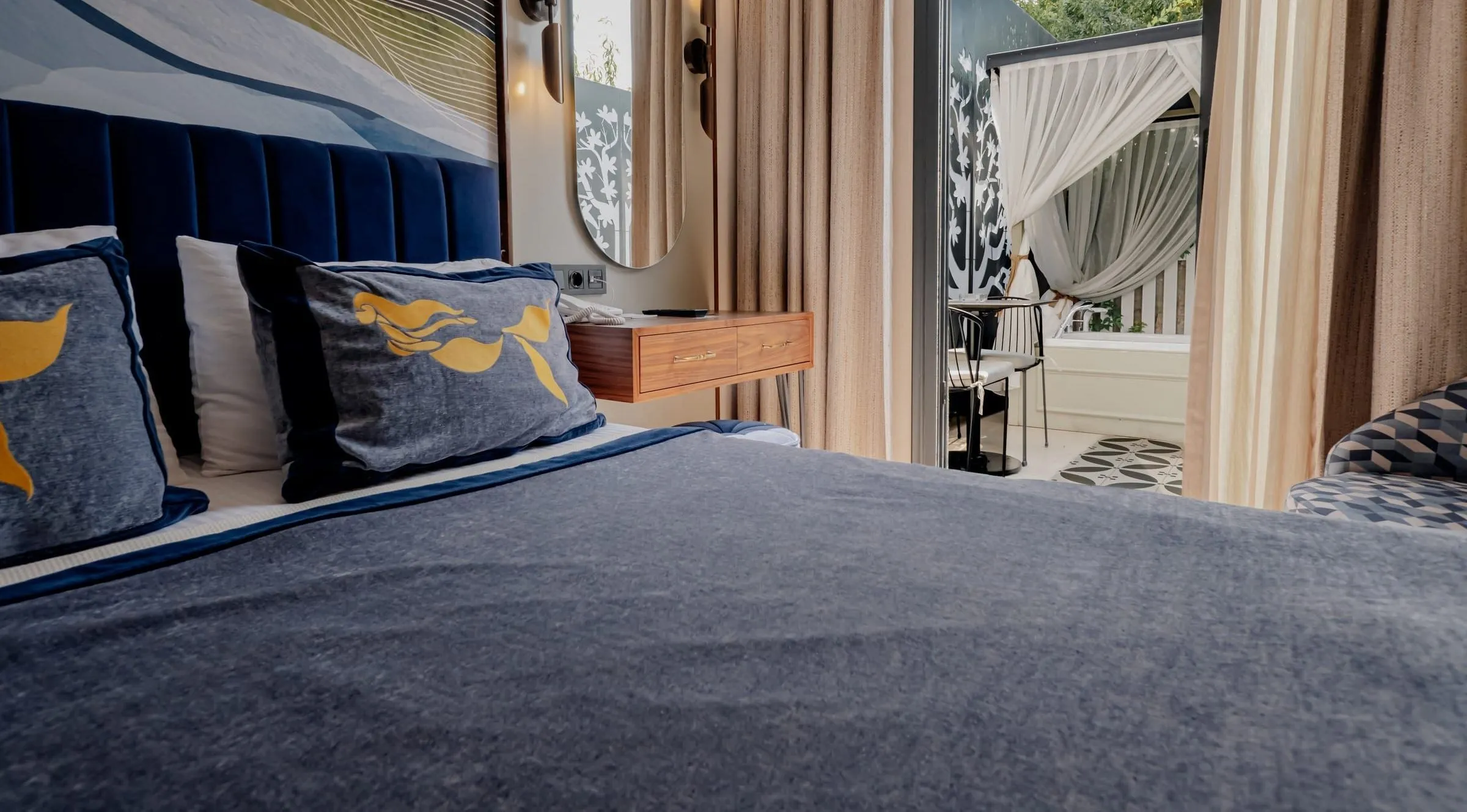 Das Bett aus niedriger Perspektive: Kissen mit Meerjungfrauenmotiv und ein Paneel mit Wellenmuster; zwischen den Vorhängen der Whirlpool unter einem Voile-Baldachin auf dem Balkon