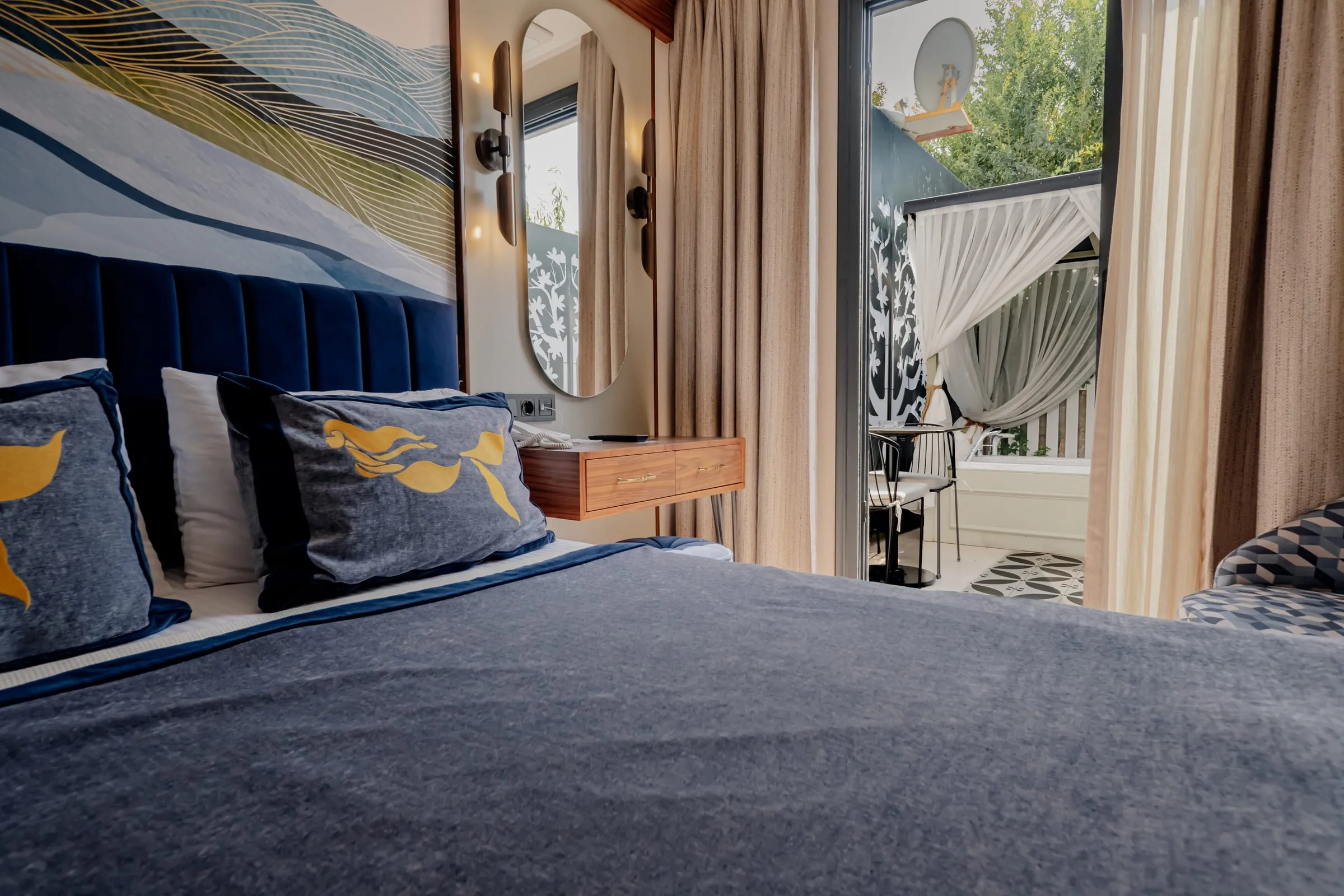 Vom Zimmer zur Terrasse: das Bett, das Wellen-Wandbild, ein ovaler Spiegel und hinter der offenen Tür das Voile